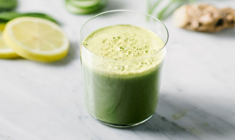 A green smoothie in a glass with lemon and ginger
