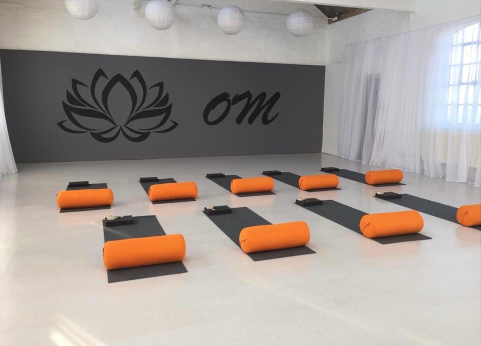 Mats set out with orange bolsters and blocks in front of the lotus and om wall