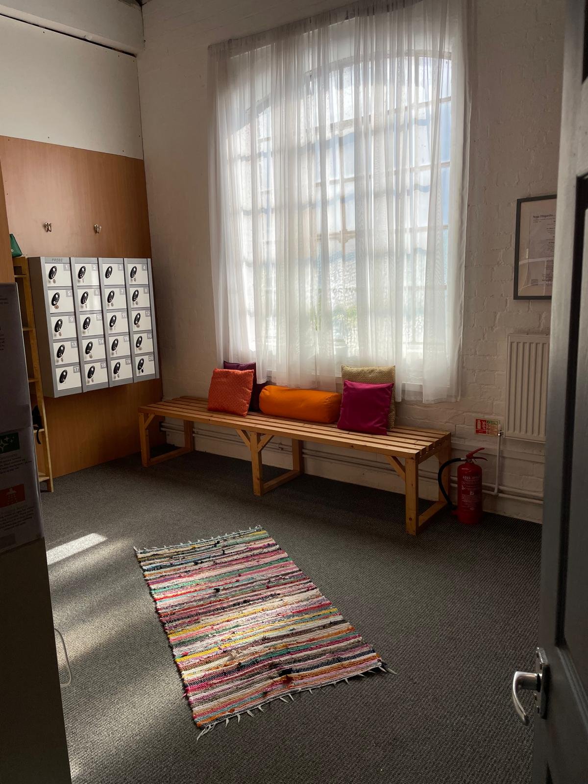 The changing room, with lockers, a bench and cushions under a tall window