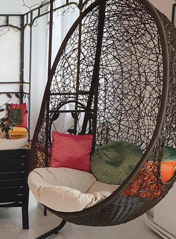A hanging wicker chair with pink, green and orange cushions