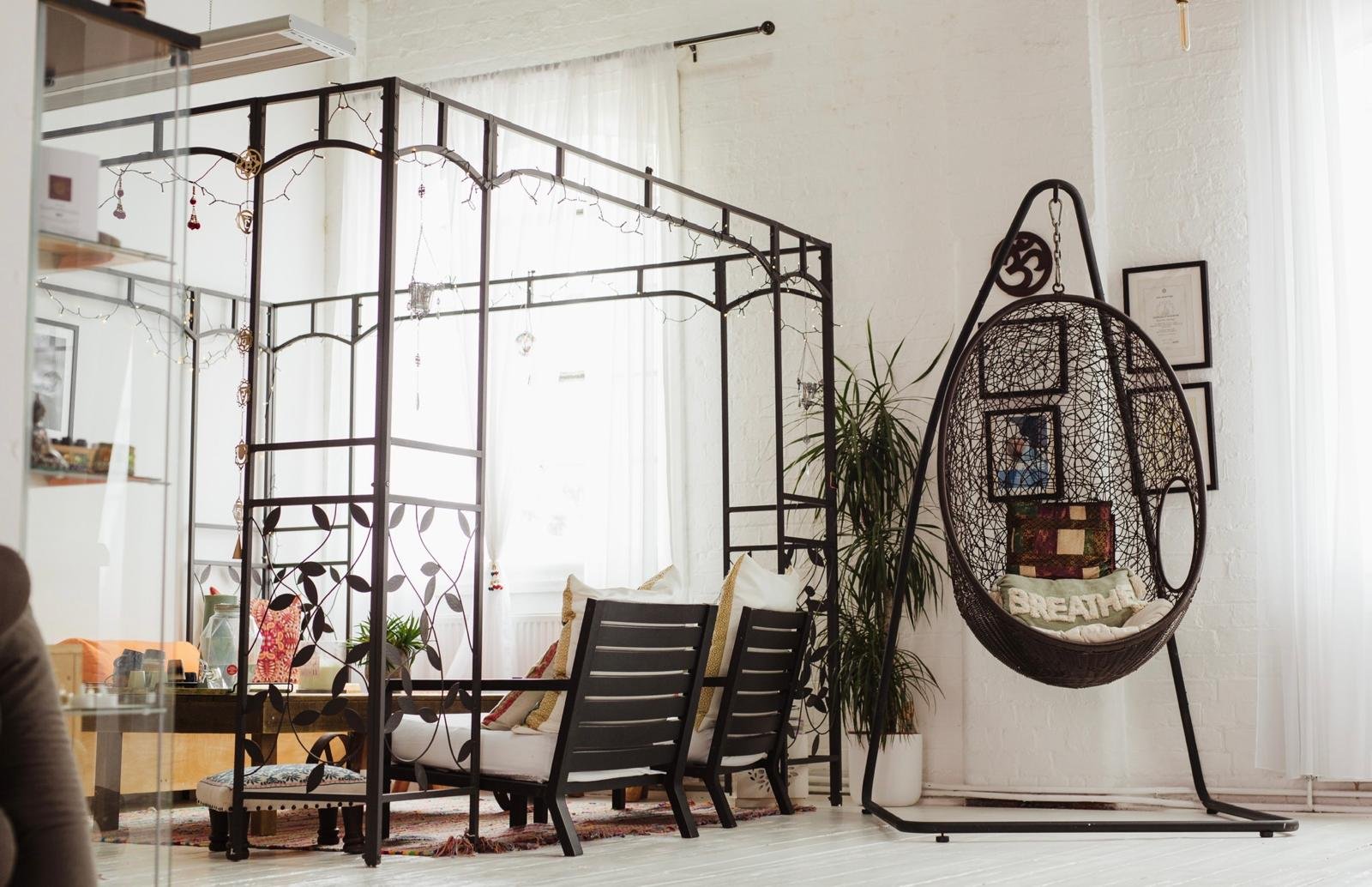 Armchairs under a black iron pergola with fairy lights, beside a hanging chair